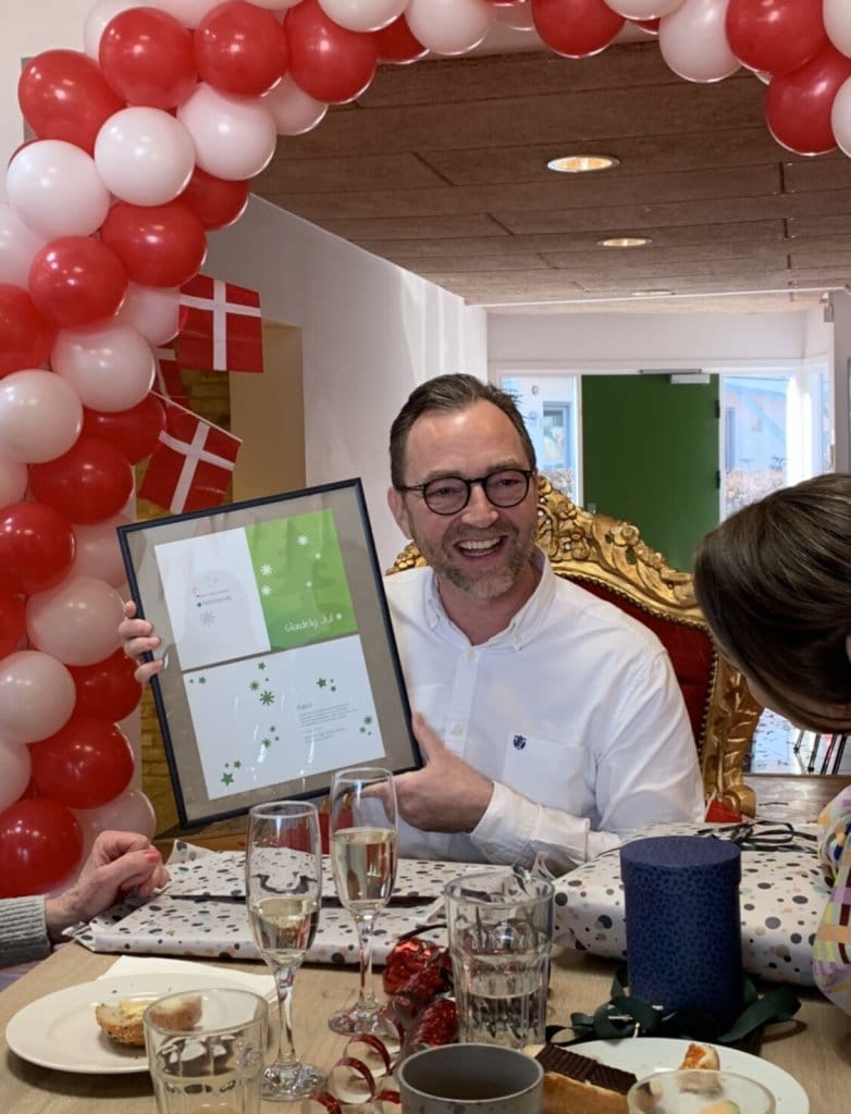 Soren Arnsbo holding a framed certificate at a celebration table with red and white Danish flag balloons